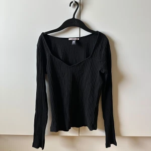 Svart ribbad långärmad topp Anna Field - Svart ribbad långärmad topp från Anna Field med snygg v-ringning. Toppen är i stretchigt material och har en figurnära passform som sitter riktigt snyggt. Perfekt att styla med jeans eller kjol för en clean look.