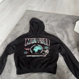 Svart NASA hoodie från H&M Divided XS - Cool svart hoodie från H&M Divided i storlek XS med stort NASA-tryck framtill, astronaut och jordklot i turkos och vitt. Tröjan har huva med snörning och långa ärmar. Perfekt för dig som gillar rymd och streetstyle.
