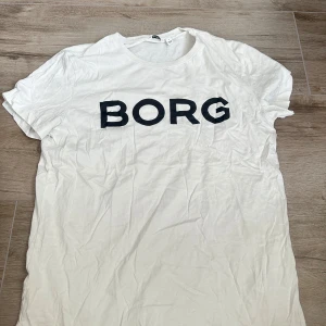 Vit Björn Borg t-shirt med tryck - Vit t-shirt från Björn Borg i mjuk bomull med svart BORG-tryck över bröstet. Klassisk rund halsringning och korta ärmar. Perfekt för en clean och sportig look.