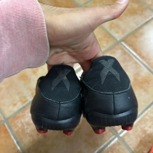 Adidas X röda och svarta fotbollsskor - Säljer ett par Adidas X fotbollsskor i rött och svart med diskret mönster och klassisk X-logga på hälen. Skorna har låg profil, platt sula med dobbar och är tillverkade i syntetmaterial för lätt känsla på planen.
