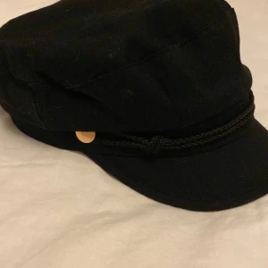 Svart skepparmössa från KappAhl - Stilren svart skepparmössa från KappAhl i klassisk modell med dekorativt snöre och guldiga knappar vid sidorna💗💗 Använt en eller två gånger💗 Pris går att diskutera💗