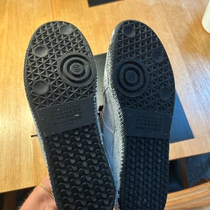 Maison Margiela sneakers i svart och vitt - Unika sneakers från Maison Margiela med handmålat svartvitt mönster och svarta skosnören. Skorna har rund tå, platt sula och är tillverkade i skinn. Perfekta för dig som vill sticka ut med en konstnärlig vibe. Givetvis autentiska använda 2 gånger 