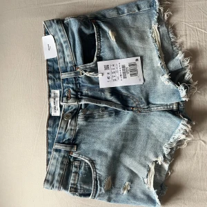 Ljusblå jeansshorts Pull&Bear - Snygga ljusblå jeansshorts från Pull&Bear med fransiga kanter och slitna detaljer. Klassisk femficksmodell med knappgylf och bälteshällor. Perfekta för en chill sommarlook.