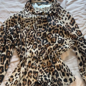 Leopardmönstrad skjorta från Zara - Snygg långärmad skjorta från Zara med leopardmönster. Skjortan har klassisk krage, knappar framtill och ett smalt knytband i midjan för extra stilpoäng.