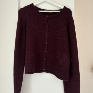 Vinröd kofta från Gina Tricot XL - Mysig vinröd kofta från Gina Tricot i storlek XL. Koftan har rund hals, långa ärmar och knappar hela vägen framtill. Materialet är fluffigt och stickat, perfekt för kyliga dagar. Enkel och stilren design som funkar till många outfits.