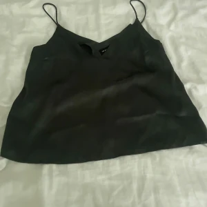 Mörkgrön satin linnetopp med smala axelband - Snygg mörkgrön linnetopp i satin med smala axelband och v-ringad hals. Toppen har en slät och glansig yta som ger en cool vibe. Perfekt att styla med jeans eller kjol för en trendig look.