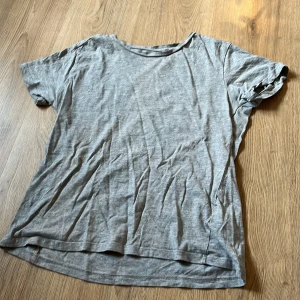 Grå basic t-shirt i bomull - En enkel grå t-shirt med rund hals och korta ärmar. Tillverkad i mjuk bomull, perfekt för chill dagar eller att matcha med jeans. Modellen är normal passform och har en clean look utan mönster eller detaljer. Den är från lager 157 men är knappt använd. 