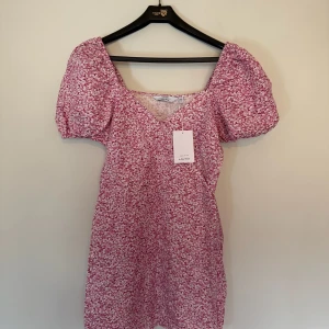 Rosa blommig kortklänning & Other Stories - Rosa klänning från & Other Stories med vitt blommigt mönster. Klänningen har puffiga korta ärmar, v-ringad hals och figurnära passform. Helt oanvänd med prislapp kvar! Strl.38, nypris: 590:-