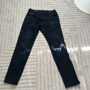 Replay Anbass svarta jeans herr - Svarta Replay Anbass jeans med slim passform och klassisk femficksdesign. Snygga detaljer med Replay-logga på myntfickan och svarta sömmar. Stretchigt material för extra komfort och stilren look. Perfekta för dig som gillar en modern och smal siluett.