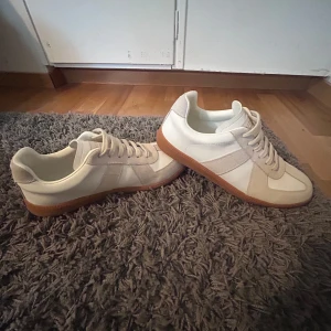 Maison Margiela sneakers beige - Maison Margiela sneakers i beige och vitt med klassisk gummisula i brunt. Skorna har snygga paneler i mocka och skinn, rund tå och platt sula. De har snörning och kommer med vita dustbags. Perfekt för dig som gillar minimalistisk och clean stil.Pris kan diskuteras!