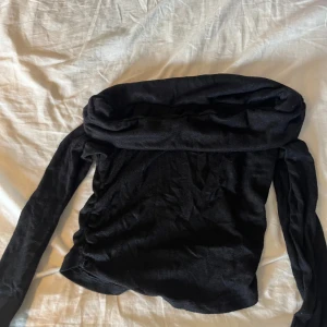 Svart offshoulder topp med långa ärmar - Snygg svart offshoulder topp med långa ärmar och en bred krage som vilar över axlarna. Perfekt för dig som vill ha en stilren och trendig look. Tunnare material som känns mjukt mot huden och sitter tajt över kroppen.