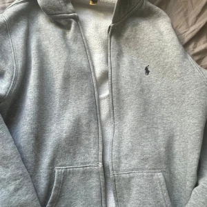 Grå hoodie från Polo Ralph Lauren XL 170/88 Billig - Säljer en grå hoodie från Polo Ralph Lauren i storlek XL barn. Zip och allt. Den har en svart liten fläck på ena sidan annars typ som ny. Billigt!