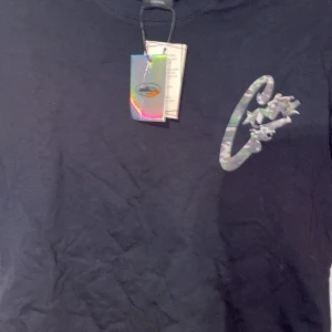 Svart t-shirt med camo-tryck - Svart t-shirt i storlek small med ett stort camouflagemönstrat tryck på både bröstet och ryggen. Rund hals och korta ärmar. Materialet känns som mjuk bomull, perfekt för dig som gillar streetwear och grafiska prints.