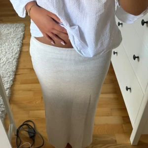 Ljusbeige lång stickad kjol - Säljer en ljusbeige långkjol i mjukt stickat material. Kjolen har en rak och slim passform som sitter snyggt över höfterna och faller rakt ner mot anklarna. Perfekt för dig som gillar stilrena och enkla plagg med en chill vibe.
