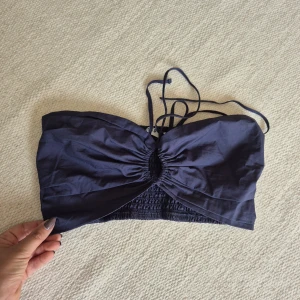 Mörkblå bandeau tubtopp från NA-KD - Snygg mörkblå bandeau tubtopp från NA-KD med smockad baksida och cool snörning framtill. Toppen är axelbandslös och har en liten cut-out detalj i mitten. Perfekt för dig som vill ha en trendig och stilren look i sommar.