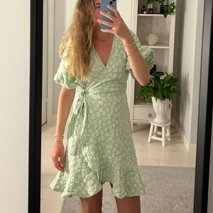 Klänning - Söt ljusgrön kort omlottklänning med vitt blommigt mönster. Helt ny