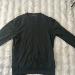 Oscar Jacobson Knit - En stilren mörkgrön tröja från Oscar Jacobson i mjuk bomull. Rund hals med ribbad kant och långa ärmar. Passformen är normal och tröjan är enkel att matcha med jeans eller andra plagg. Perfekt för dig som gillar minimalistisk och clean stil.