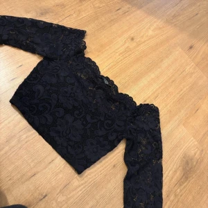 Svart spets  - Säljer en svart off shoulder topp från NLY One i storlek XS. Toppen har långa ärmar och är helt täckt av blommig spets med fina detaljer och vågig kant upptill. 