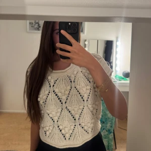 Vit stickad kortärmad topp - Superfin vit stickad topp med korta ärmar och unikt hålmönster i geometriska former. Croppad modell som ger en trendig vibe och passar perfekt till både jeans och kjol. Mjuk och bekväm, perfekt för vår och sommar.