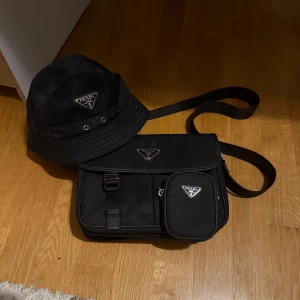 Prada Set (Väska + Bucket Hat) - Säljer ett Prada sett jag haft ett tag. Väska, mini väska och bucket hat. Bucket haten är för liten för mig och har inte använt den mycket. 