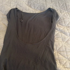 Mörkgrå basic linnetopp med djup öppen rygg - En mörkgrå, enkel linnetopp med djup rund öppen rygg. Toppen är kort T-shirt ärmad och har en smal passform som sitter snyggt mot kroppen. Materialet känns mjukt och stretchigt, perfekt för att matcha med jeans eller kjol. Stilren och lätt att styla.