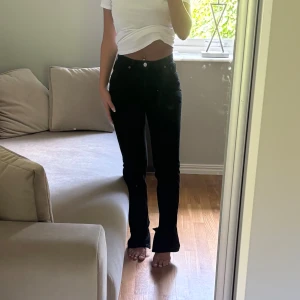 Svarta bootcut jeans med hög midja - Snygga svarta jeans med bootcut passform och hög midja. Klassisk femficksmodell med knapp och dragkedja framtill. Jeansen har en rak siluett upptill och lätt utsvängda ben, vilket ger en cool och tidlös look.