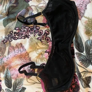 Svart meshbh från Lounge - Säljer en svart bh från Lounge i mesh med diskret logga i tyget. Toppen har justerbara axelband och metallringar för extra detalj. 