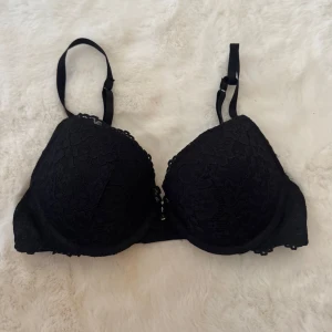 Svart spetsig BH från H&M - Snygg svart BH från H&M med spetsdetaljer och justerbara axelband. Kuporna är vadderade och har ett feminint blommigt spetsmönster. Materialet är mjukt och stretchigt med 89% polyamid och 11% elastan för skön passform.