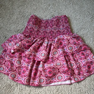 Rosa mönstrad volangkjol - Supersöt kort kjol med volanger och ribbad  midja. Materialet är pollyester med ett mjukt innerfoder. Perfekt för sommaren och för dig som gillar färg.