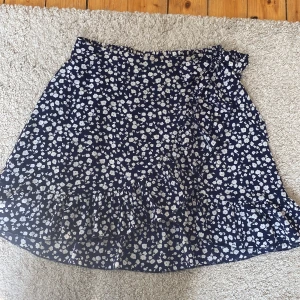 Blommig omlottkjol - Supersöt omlottkjol från Shein i marinblått med vitt blommönster. Kjolen har volang längs nederkanten och knyt i sidan för extra detalj.