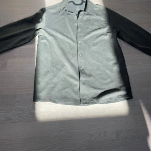 Grå skjorta med knappar från Knowledge Cotton - Snygg grå skjorta från Knowledge Cotton med klassisk krage och långa ärmar. Skjortan har en stilren look med knappar hela vägen och diskret logga på bröstet. Materialet är mjukt och känns som bomull.