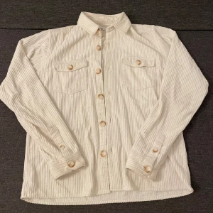 Vit randig skjorta från Ciszere - Snygg vit skjorta från Ciszere i slim fit med diskreta vertikala ränder. Tillverkad i 100% bomull, har klassisk krage, långa ärmar och knappar framtill samt två bröstfickor med knapp. Perfekt för dig som gillar stilrena detaljer.