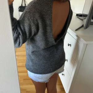 Grå stickad tröja med öppen rygg - Mysig grå stickad tröja med breda ärmar och en riktigt snygg öppen rygg. Passar till jeans eller shorts och har en loose fit som känns avslappnad.