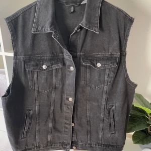 Svart jeansväst med råa kanter - Cool svart jeansväst från H&M med råa, avklippta ärmkanter och klassisk krage. Västen har två bröstfickor med knappar och två sidofickor. Perfekt att slänga över en hoodie eller t-shirt för en avslappnad look. Storleken är XL men den är oversized så en rymlig XL.