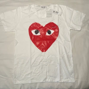 CDG tröja med hjärta  - Säljer en vit t-shirt från Comme des Garçons Play med det ikoniska röda hjärtat med ögon tryckt på bröstet. T-shirten har rund hals, korta ärmar och är gjord i mjuk bomull. Perfekt statement-plagg för dig som gillar coola designer och streetstyle.