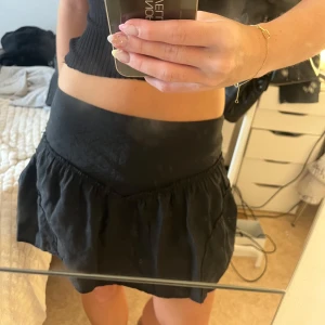 Svart volangkjol från Zara - Supersöt svart kortkjol från Zara med bred midja och volangdetaljer. Kjolen har en lätt rynkad struktur som ger en cool och feminin vibe. Perfekt att matcha med en crop top eller stickad tröja. Materialet känns mjukt och lätt mot huden.