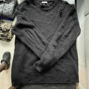 Svart stickad tröja med slitna detaljer - Svart stickad tröja från Zara Man med coola slitna detaljer och grov ribbad struktur. Tröjan har rund hals och långa ärmar, perfekt för dig som gillar en edgy och avslappnad stil. Passar dig som vill ha en basic med lite extra attityd.