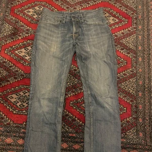 Levis 501 ljusblå jeans straight fit - Klassiska Levis 501 jeans i ljusblå tvätt med raka ben och normal passform. Jeansen har fem fickor, knappgylf och tydliga Levis-detaljer som röd etikett och patch bak. Perfekta för en avslappnad och tidlös stil.