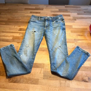 Ljusblå slitna jeans med skinny fit - Säljer ett par ljusblå jeans med skinny passform och slitna detaljer framtill. Jeansen har klassisk femficksdesign, dragkedjegylf och snygg tvättad look. Perfekta för dig som gillar en avslappnad och trendig stil.