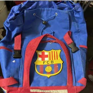 FC Barcelona ryggsäck blå och röd - Säljer en FC Barcelona ryggsäck i blått och rött med klubbens emblem framtill. Väskan har justerbara axelremmar, snörning upptill och flera fack med dragkedja. Materialet är slitstark polyester och designen är perfekt för dig som älskar fotboll. Lite smutsig men tvättar innan skick