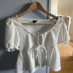 Vit blus med knyt från Gina Tricot - Supersöt vit blus från Gina Tricot i storlek XS. Den har puffiga korta ärmar med volangkant, två knyt framtill och en lätt rynkad struktur i tyget. . Jag köpte den här i början av förra sommaren, jag har testat den men tyckte inte den passade mig så har aldrig använt den (förutom att testa då). Säljer bara för jag som sagt inte tyckte den såg så bra ut på mig. Köpte för 280 men säljer för 80 (kan diskuteras)