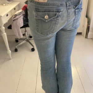 Ljusa true religion jeans utsvängda -  True Religion jeans – ljusa, utsvängda Snygga och bekväma jeans från True Religion. Väl använda men i ganska bra skick. Sitter jättebra på mig som är 173 cm, storleken motsvarar ca EU 28 •Lagning gjord av skräddare mellan benen, knappt synlig.                                                  •Knapp till bakfickan finns, behöver sys fast • Mindre reva på knät & några små fläckar (kan ev. försvinna i tvätt) Pris kan diskuteras och tveka inte att fråga efter fler bilder eller om du har någon fråga