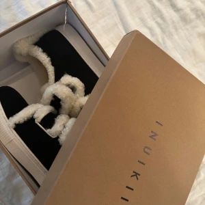 Svarta sneakers från Inuikii - Intressekoll!                                                            Unika svarta Inuikii sneakers med fluffig vit pälsdetalj och breda pälsbeklädda remmar. Skorna har rund tå, platt sula och är tillverkade i mocka med inslag av päls för extra cozy vibe. Perfekta för dig som vill sticka ut med en cool vinterlook. Säljer för  2200kr på Vinted .