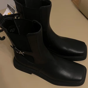 Svarta boots med spänne - Snygga svarta boots med fyrkantig tå och dekorativt spänne på sidan. Perfekta för en stilren look. Storek 41 oanvända 