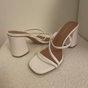 Vita klackskor från Boohoo - Snygga vita klackskor från Boohoo med smala remmar och en fyrkantig tå. Perfekta för att lyfta din stil med en elegant touch. Klacken är bred och stabil, vilket ger extra komfort.