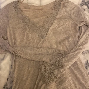 Beige långärmad tröja från intimissimi - Säljer en beige långärmad tröja med v-ringning och vackra spetsdetaljer vid halsen och ärmsluten. Perfekt för en stilren och elegant look. Tröjan är mjuk och bekväm, idealisk för både vardag och speciella tillfällen.