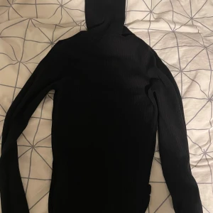 Svart ribbad polotröja - Säljer en stilren svart ribbad polotröja med långa ärmar. Perfekt för kyligare dagar och ger en snygg och elegant look. Passar bra till både jeans och kjol.