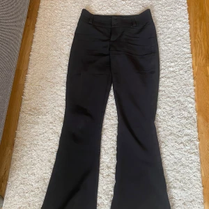 Svarta byxor med bootcut - Snygga svarta byxor med bootcut-stil och hög midja. Byxorna har två bakfickor med knappar och en stilren design som passar perfekt för en trendig look. Dem ska såklart tvättas innan jag skickar dem. Dem var väldigt små i midjan även om dem är i storlek S. Jag säljer dem för att dem är för små även om jag har storlek Xs 