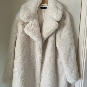 Lång Vit pälsjacka! - Säljer en supermjuk och fluffig lång vit pälsjacka från Gina Tricot. Jackan har en stor krage och är perfekt för att hålla sig varm under kyliga dagar. Den har en klassisk design som funkar till många olika outfits. Storlek 40