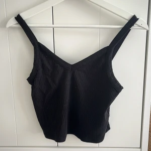 Svart ribbad linnetopp - Snygg svart ribbad linnetopp med breda axelband och v-ringning. Perfekt för en stilren look.